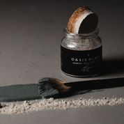 A jar of the Oasis Black Mineral Clay Mud Mask in Byron, with a line of the powder and a line of the activated mask on a grey surface. Byron is a stormy turquoise coloured mask featuring French Green Clay, Spirulina, Blue Butterfly Pea Flower, Lemon Myrtle and Black Seeds. Available exclusively from Oasis Black - makers of All Natural and Organic Botanical Skincare featuring Black Seeds (Nigella Sativa). Handmade in small batches to waterless formulations in the Byron Bay Hinterland. 