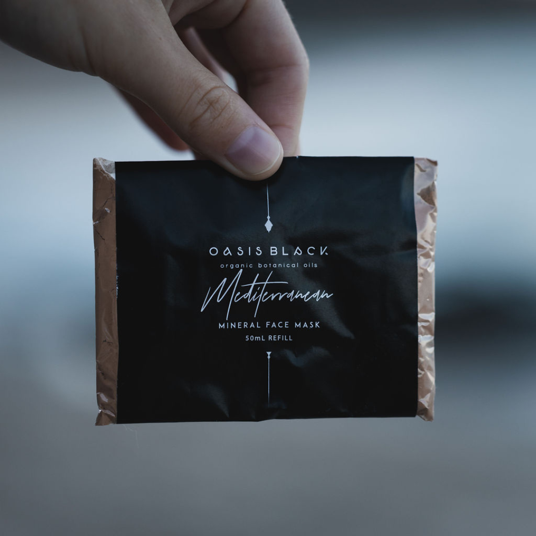 Hand holding a plastic free & home compostable sachet of Oasis Black's Powdered Clay Facial Mask in Mediterranean. Mediterranean is a terracotta coloured mask activated with water and featuring Mediterranean Clays, Rose Petals, Hibiscus, Aloe Vera, Calendula and Black Seeds. Available exclusively from Oasis Black - makers of All Natural and Organic Botanical Skincare featuring Black Seeds (Nigella Sativa). Handmade in small batches to waterless formulations in the Byron Bay Hinterland. 