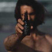 100% Organic and All Natural Face & Body Oil Featuring Black Seed Oil – MOROCCAN – Scent inspired by Morocco packaged in 100ml Amber Glass Bottle pictured being held up in front of a man’s face - Non Greasy, Multi-Purpose, Fast Absorbing, Vegan Friendly, Nutrient Dense, Eco-friendly, Sustainable, Waterless and Unisex Skincare Oils made by Oasis Black – Organic Botanical Skincare - Born in Morocco, Made in small handmade batches in the Byron Bay region