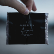 Hand holding a plastic free & home compostable sachet of Oasis Black's Powdered Clay Mud Mask in Amazonian. Amazonian is a purple coloured facial mask activated with water featuring Amazonian Clays, Acai, Maca, Inca berries, Camu Camu and Black Seeds. Available exclusively from Oasis Black - makers of All Natural and Organic Botanical Skincare featuring Black Seeds (Nigella Sativa). All products are handmade in small batches to waterless formulations in the Byron Bay hinterland. 