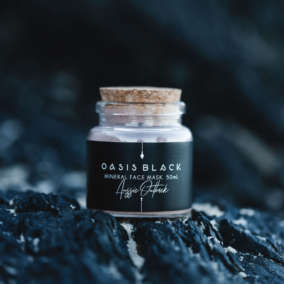 Glass jar (with a cork lid) of Oasis Black Mineral Facial Mask in Aussie Outback on a dark rocky background. Aussie Outback is a red dirt coloured facial mask activated with water featuring Australian Clays, Davidson Plum, Lemon Myrtle, Muntrie, Kakadu Plum & Black Seeds. Available exclusively from Oasis Black - makers of All Natural and Organic Botanical Skincare featuring Black Seeds (Nigella Sativa). All products are handmade in small batches to waterless formulations in the Byron Bay hinterland