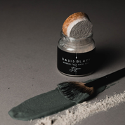 A jar of the Oasis Black Mineral Clay Mud Mask in Byron, with a line of the powder and a line of the activated mask on a grey surface. Byron is a stormy turquoise coloured mask featuring French Green Clay, Spirulina, Blue Butterfly Pea Flower, Lemon Myrtle and Black Seeds. Available exclusively from Oasis Black - makers of All Natural and Organic Botanical Skincare featuring Black Seeds (Nigella Sativa). Handmade in small batches to waterless formulations in the Byron Bay Hinterland. 