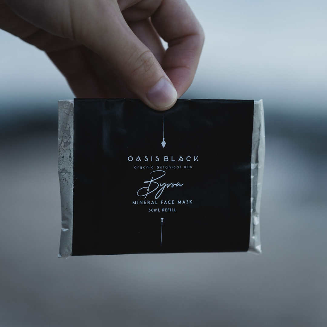 Hand holding a plastic free & home compostable sachet of Oasis Black's Powdered Clay Facial Mask in Byron. Byron is a stormy turquoise coloured mask featuring French Green Clay, Spirulina, Blue Butterfly Pea Flower, Lemon Myrtle and Black Seeds. Available exclusively from Oasis Black - makers of All Natural and Organic Botanical Skincare featuring Black Seeds (Nigella Sativa). Handmade in small batches to waterless formulations in the Byron Bay Hinterland. 