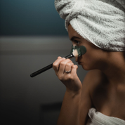 Side view of a woman applying a green facial mask with a brush, wearing a towel on her head. The mask is Oasis Black's Mineral Clay Mud Mask in Byron - a stormy turquoise coloured mask featuring French Green Clay, Spirulina, Blue Butterfly Pea Flower, Lemon Myrtle and Black Seeds. Available exclusively from Oasis Black - makers of All Natural and Organic Botanical Skincare featuring Black Seeds (Nigella Sativa). Handmade in small batches to waterless formulations in the Byron Bay Hinterland.