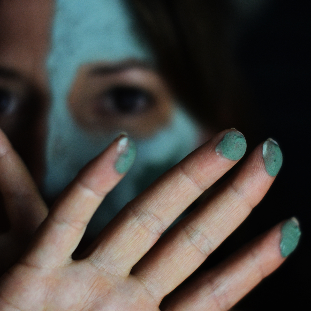 Close up of a person's hand with the Oasis Black Mineral Clay Mud Mask in Byron on their fingertips, the person's face in the background. Byron is a stormy turquoise coloured mask featuring French Green Clay, Spirulina, Blue Butterfly Pea Flower, Lemon Myrtle and Black Seeds. Available exclusively from Oasis Black - makers of All Natural and Organic Botanical Skincare featuring Black Seeds (Nigella Sativa). All products are handmade in small batches to waterless formulations in the Byron Bay hinterland. 