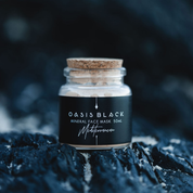 Glass jar (with a cork lid) of Oasis Black Mineral Facial Mask in Mediterranean on a dark rocky background. Mediterranean is a terracotta coloured mask activated with water and featuring Mediterranean Clays, Rose Petals, Hibiscus, Aloe Vera, Calendula and Black Seeds. Available exclusively from Oasis Black - makers of All Natural and Organic Botanical Skincare featuring Black Seeds (Nigella Sativa). Handmade in small batches to waterless formulations in the Byron Bay Hinterland. 