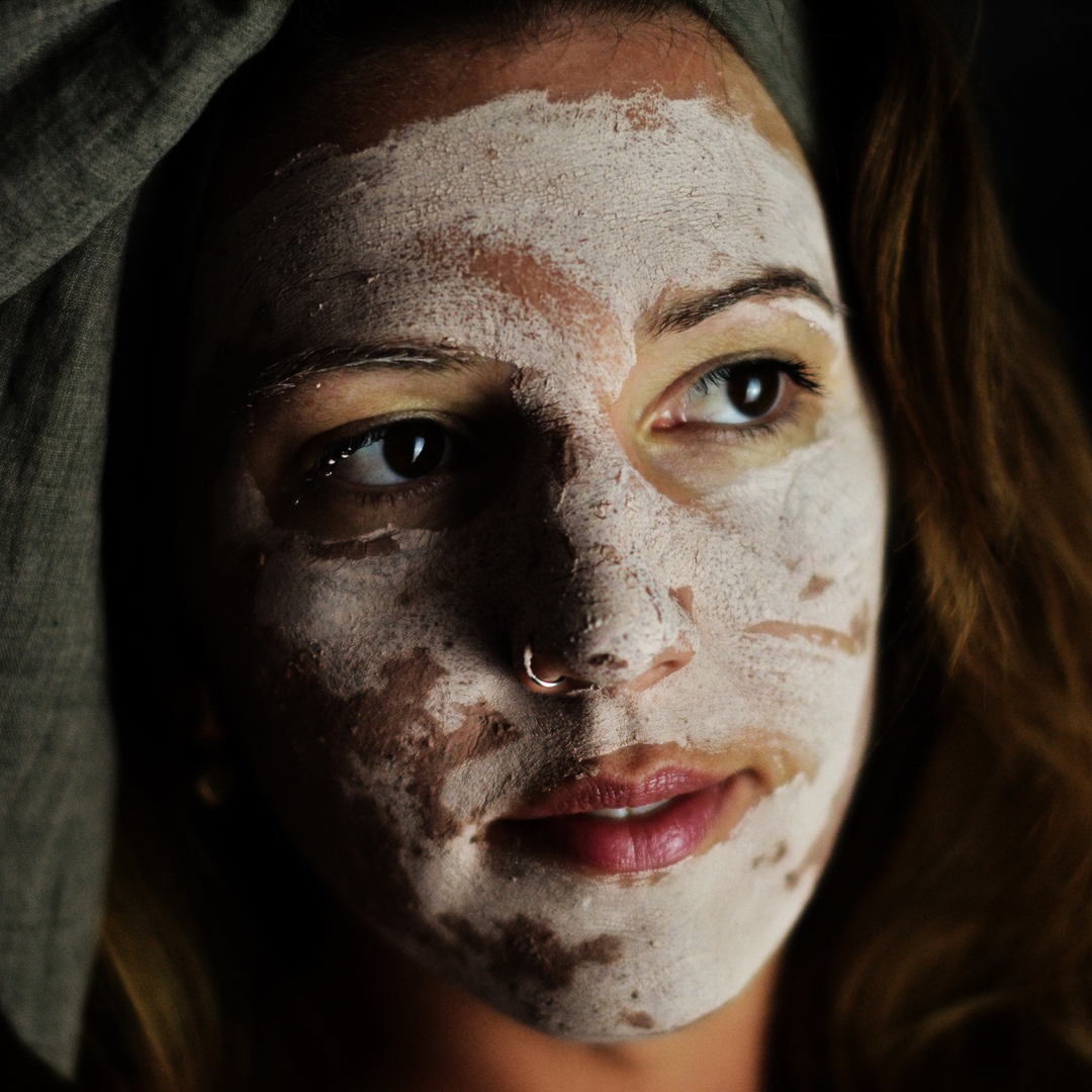 A woman's face with the Oasis Black Mineral Clay Mud Mask in Nude applied and drying. Nude is a pink coloured facial mask activated with water featuring French Pink Clay, Australian Clays, Aloe Vera, Chamomile, Rose petals and Black Seeds. Available exclusively from Oasis Black - makers of All Natural and Organic Botanical Skincare featuring Black Seeds (Nigella Sativa). All products are handmade in small batches to waterless formulations in the Byron Bay hinterland