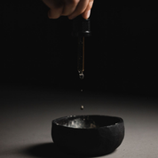 Glass dropper with Oasis Black Face & Body Oil being dropped into a black clay mixing bowl against a dark background. Available exclusively from Oasis Black - makers of All Natural and Organic Botanical Skincare featuring Black Seeds (Nigella Sativa). Handmade in small batches to waterless formulations in the Byron Bay Hinterland.