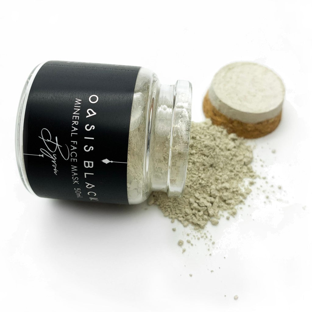 Oasis Black Byron Mineral Clay Mud Mask glass jar, on it's side with light green powder spilled out and cork lid behind. Byron is a stormy turquoise coloured mask activated with water featuring French Green Clay, Spirulina, Blue Butterfly Pea Flower, Lemon Myrtle & Black Seeds. Available exclusively from Oasis Black - makers of All Natural and Organic Botanical Skincare featuring Black Seeds (Nigella Sativa). All products are handmade in small batches to waterless formulations in the Byron Bay hinterland